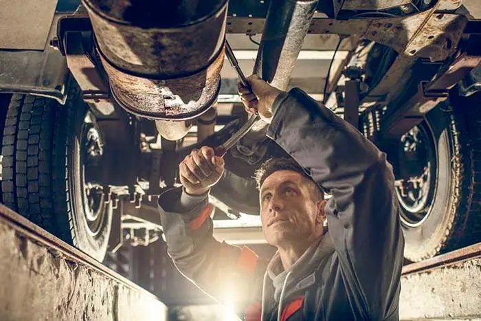 Mid adult auto mechanic working on a chassis in auto repair shop.