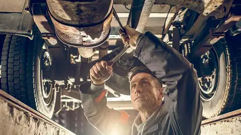 Mid adult auto mechanic working on a chassis in auto repair shop.