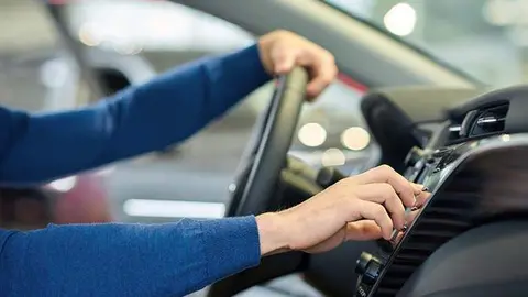 Close up of man's hands in blue sweater. Driver sitting in car and holding on his hand on steering wheel and turning on heating. Crop of well-groomed male arms when guy choosing music in auto.