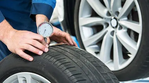 Mechanic, pressing a gauge into a tire tread to measure its depth for vehicle and road safety
