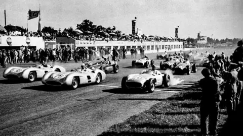 Gro&szlig;er Preis von Italien in Monza, 11.&nbsp;September 1955. Foto vom Start. Vordere Reihe, von links nach rechts: die Mercedes-Benz W&nbsp;196&nbsp;R Formel&nbsp;1-Rennwagen von Juan Manuel Fangio (Stromlinienkarosserie, Startnummer&nbsp;18, der sp&auml;tere Sieger des Rennens), Stirling Moss (Stromlinienkarosserie, Startnummer&nbsp;16) und Karl Kling (Rennwagen mit frei stehenden R&auml;dern, Startnummer&nbsp;20). Im Hintergrund: W&nbsp;196&nbsp;R mit frei stehenden R&auml;dern von Piero Taruffi (Startnummer&nbsp;14, sp&auml;ter Platz&nbsp;2). (Fotosignatur der Archive von Mercedes-Benz Classic: R7963) 

Italian Grand Prix in Monza, 11&nbsp;September 1955. Photo taken at the start of the race. Front row, from left to right: Mercedes-Benz W&nbsp;196&nbsp;R Formula&nbsp;1 racing cars of Juan Manuel Fangio (streamlined bodywork, starting number&nbsp;18, the eventual winner of the race), Stirling Moss (streamlined bodywork, starting number&nbsp;16) and Karl Kling (racing car with free-standing wheels, starting number&nbsp;20). In the background: W&nbsp;196&nbsp;R with free-standing wheels of Piero Taruffi (starting number&nbsp;14, eventually placing 2nd). (Photo index number in the Mercedes-Benz Classic Archive: R7963)